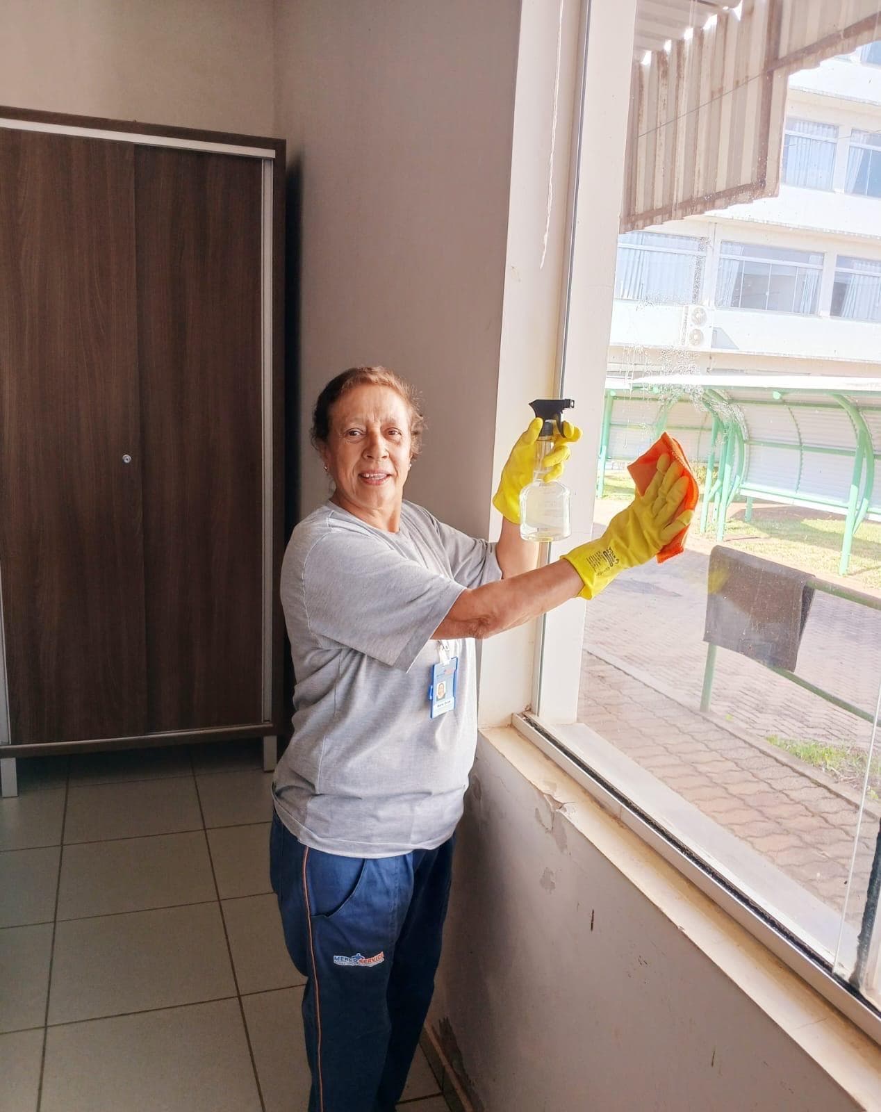 Colaboradora realizando limpeza de vidros e esquadrias
